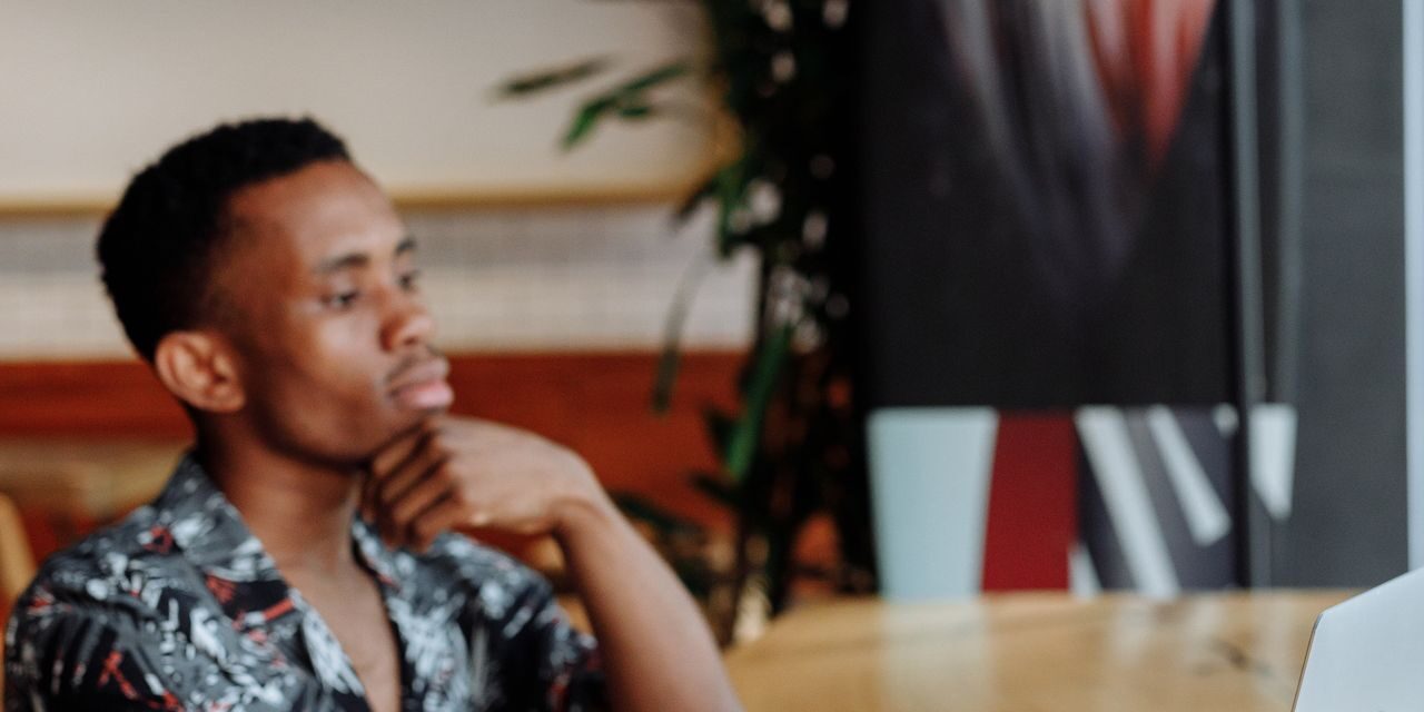 A man working thoughtfully on a laptop at a café table with coffee nearby, capturing a moment of focused reflection away from the office