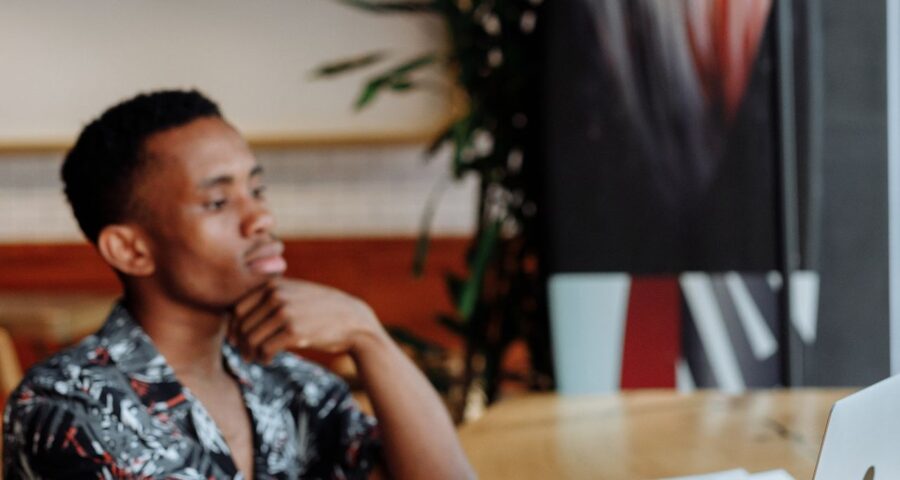 A man working thoughtfully on a laptop at a café table with coffee nearby, capturing a moment of focused reflection away from the office